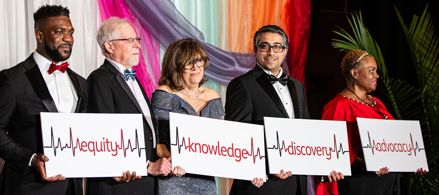Photo of four people holding up a banner reading equity, knowledge, discovery, and advocacy with each word separated by an EKG reading.
